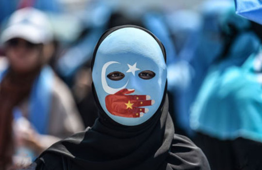 یک تظاهرکننده با ماسک منقش به پرچم شرق ترکستان و چین در اعتراض به کشتار اویغورها
