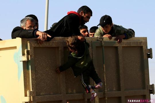 یک مرد آواره‌ی عراقی در حال پرت کردن فرزندش به بالای کامیون برای فرار از دست داعش