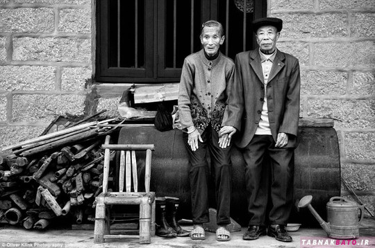 دو مرد که در مقابل خانه کوچک خود بر روی بشکه نشسته اند