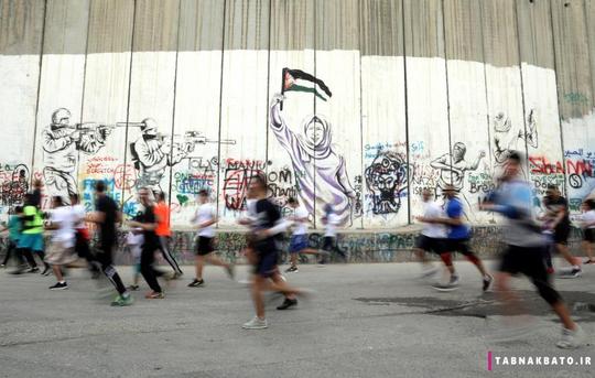 عبور شرکت کنندگان دو ماراتون از کنار دیوار حائل رژیم صهیونیستی در زمان برگزاری دو ماراتون سالانه فلسطین در شهر بیت لحم در کرانه باختری.