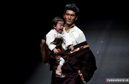 واکنش یک دختر بچه در آغوش یک مدل لباس در لحظه‌ی نمایش لباس‌های طراح تبتی به نام «ای.جی نامو» در یک فشن شو در هفته مد چین در شهر پکن.