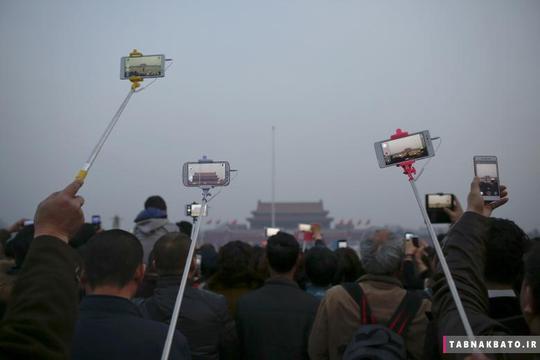 مردم در حین مراسم اهتزاز پرچم در میدان تیانانمن پکن با استفاده از اتصال تلفن‌های هوشمند به مونوپادهای سلفی، از خود عکس سلفی می‌گیرند. (3 مارس 2016)