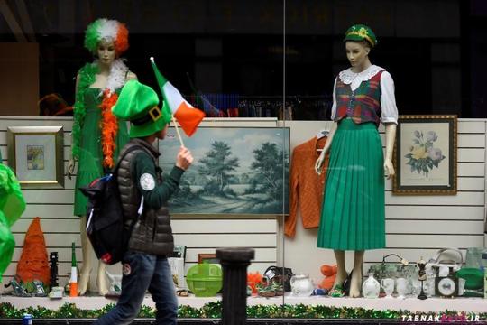 مردی در حال عبور از کنار ویترین یک مغازه در هنگام راهپیمایی روز سنت پاتریک در شهر دوبلین