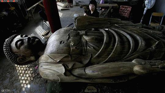 پیکر تراش اهل چین در حال تراشیدن چوب به شکل مجسمه ی غول پیکر بودا
